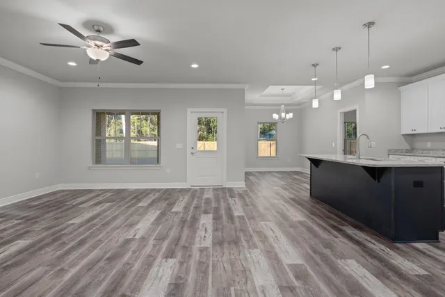 a view of an empty room with wooden floor and a kitchen