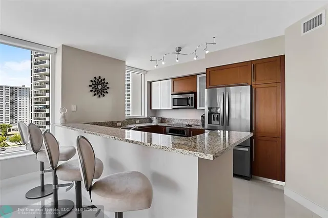 a kitchen with stainless steel appliances granite countertop a stove a refrigerator a sink dishwasher a dining table and chairs with wooden floor