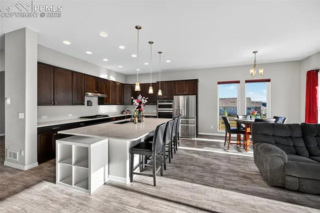 a kitchen with stainless steel appliances kitchen island granite countertop a refrigerator a stove a sink a dining table and chairs with wooden floor