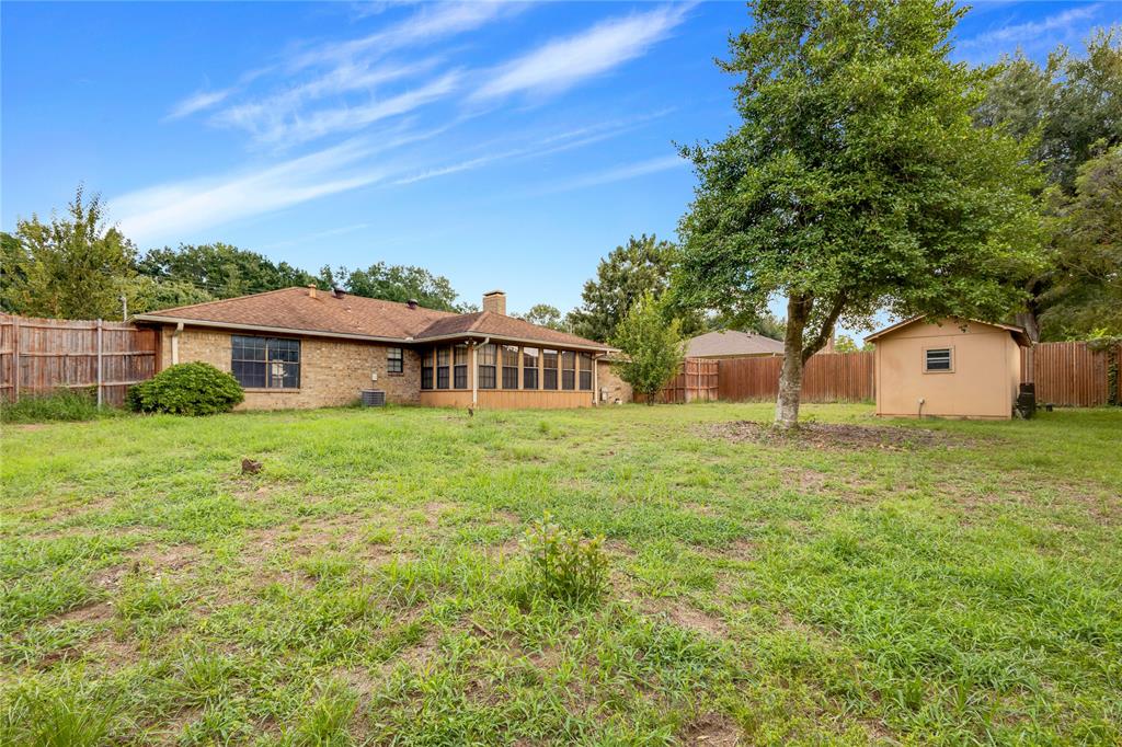 1609 Robin Street Mineola, TX 75773 - Photo 23 of 24 Expansive backyard featuring a brick exterior residence, enclosed sunroom, a separate storage shed, mature tree, and wood privacy fencing