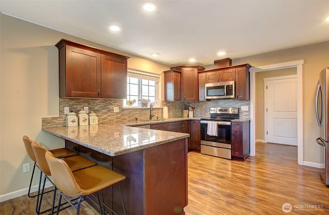 a kitchen with granite countertop a stove top oven a sink dishwasher a dining table and chairs with wooden floor