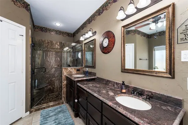 a bathroom with a granite countertop double vanity sink a mirror and a shower