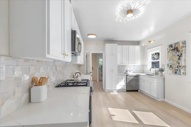 a kitchen with stainless steel appliances granite countertop a refrigerator a stove a sink and white cabinets with wooden floor