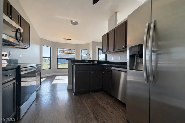 a kitchen with stainless steel appliances granite countertop a refrigerator a sink dishwasher a stove and white countertops with wooden floor