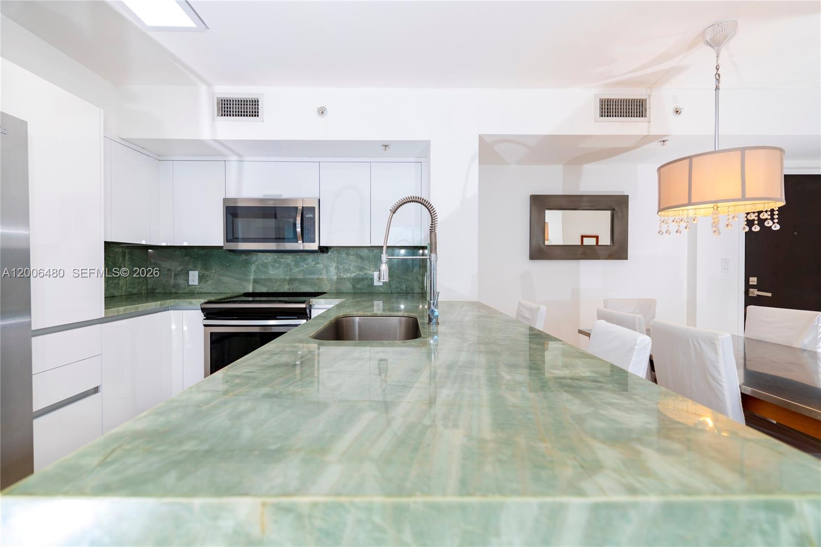 90 Alton Road, Unit 2304 Miami Beach, FL 33139 - Photo 4 of 16 a large white kitchen with stainless steel appliances granite countertop a stove a sink dishwasher and white cabinets with wooden floor
