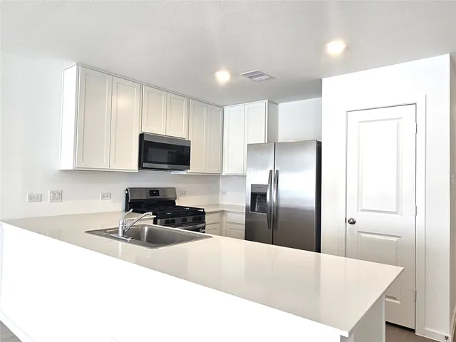 a kitchen with granite countertop a refrigerator a sink a stove a microwave a counter top space and cabinets