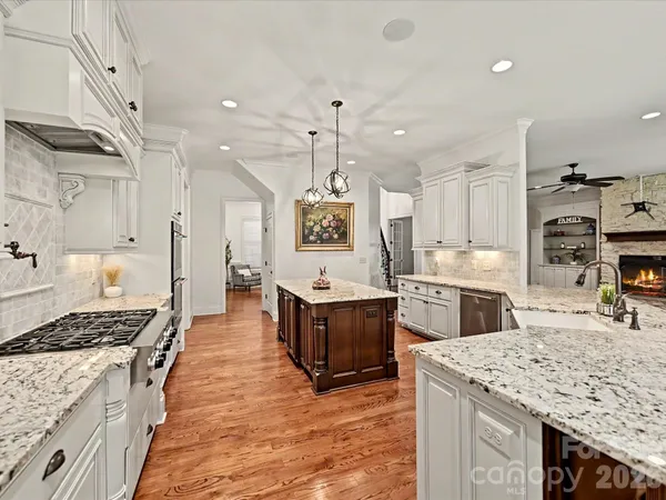 a large kitchen with stainless steel appliances kitchen island granite countertop a stove a sink dishwasher and white cabinets with wooden floor