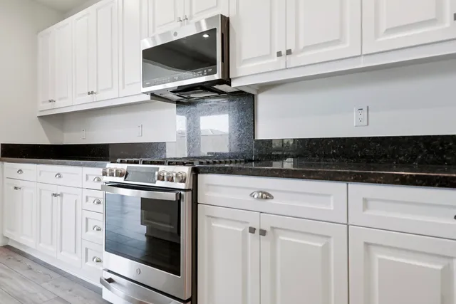 a kitchen with stainless steel appliances granite countertop white cabinets and a stove a sink