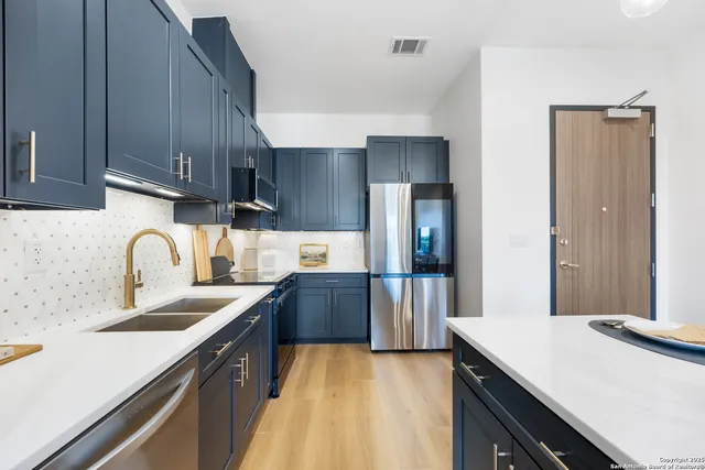 a kitchen with stainless steel appliances a sink dishwasher a refrigerator and cabinets with wooden floor