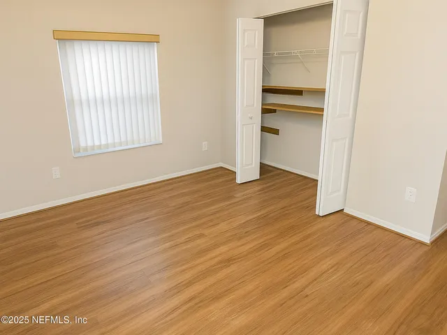 an empty room with wooden floor closet and windows