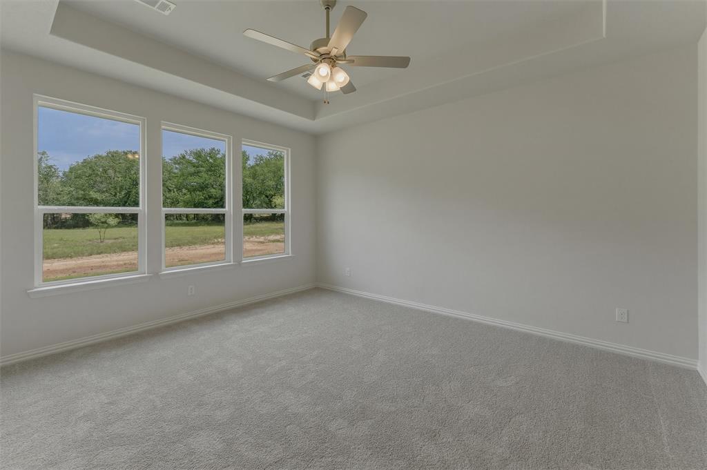 156 Oak Grv Way Springtown, TX 76082 - Photo 13 of 25 Spacious room featuring three large windows, a tray ceiling, and a ceiling fan with integrated lighting