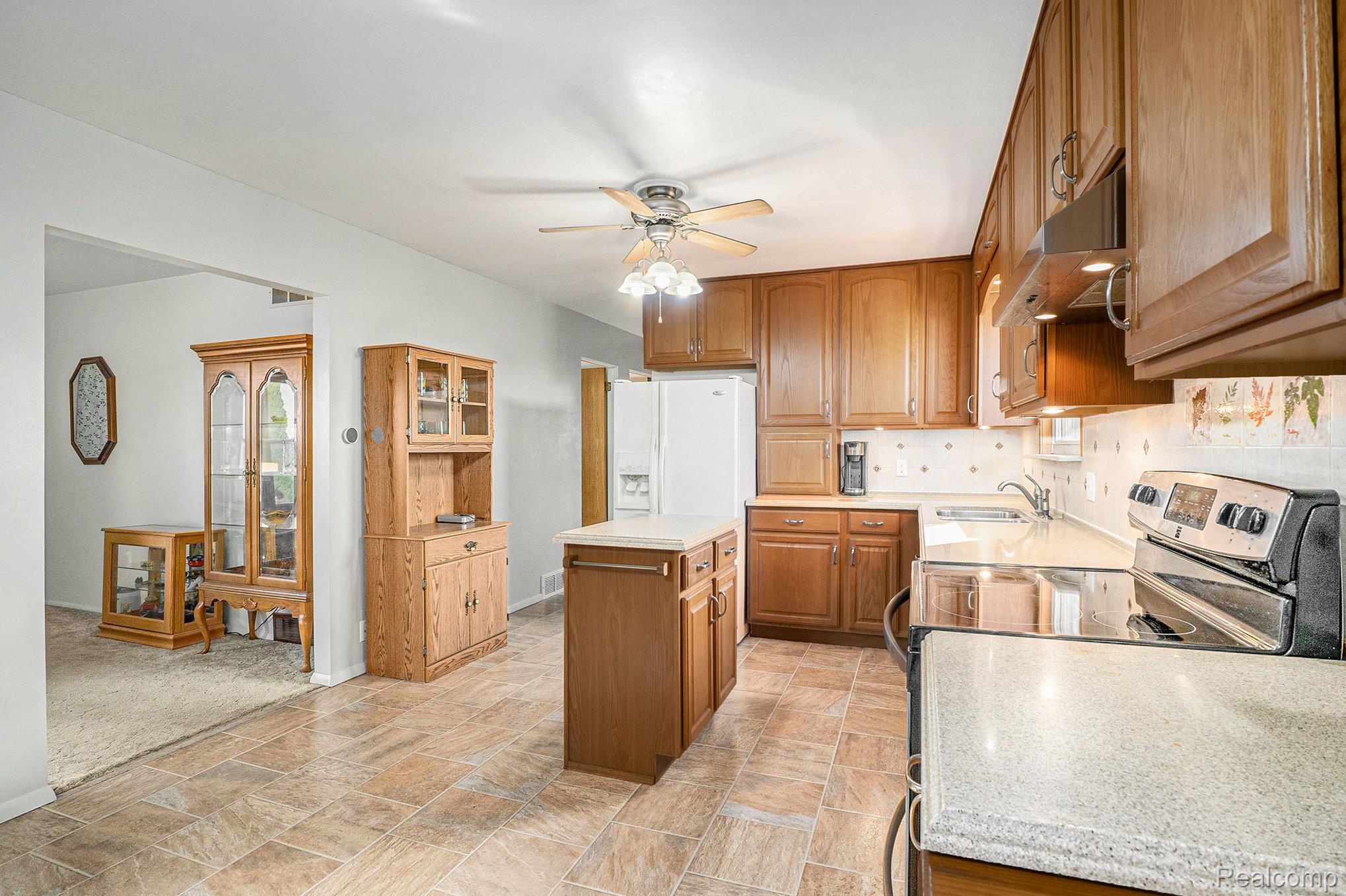 5627 West Fairgrove Road Fairgrove, MI 48733 - Photo 10 of 26 Kitchen featuring stainless steel electric stove, brown cabinets, backsplash, under cabinet range hood, and a kitchen island