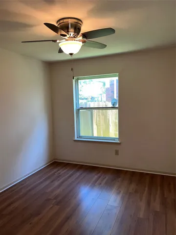 an empty room with wooden floor chandelier fan and windows