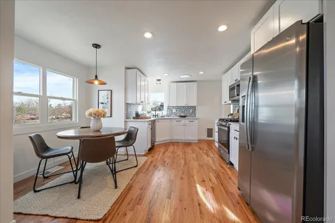 a kitchen with stainless steel appliances granite countertop a refrigerator a sink a stove and white cabinets with wooden floor