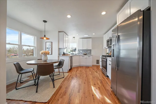 a kitchen with stainless steel appliances granite countertop a refrigerator a sink a stove and white cabinets with wooden floor