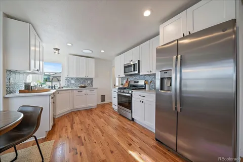 a kitchen with a refrigerator a sink a stove top oven a kitchen island and chairs with wooden floor