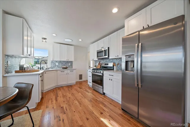 a kitchen with a refrigerator a sink a stove top oven a kitchen island and chairs with wooden floor