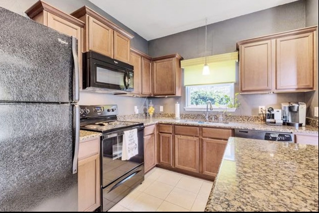 13405 Clara Martin Road Manor, TX 78653 - Photo 7 of 26 Kitchen featuring black appliances, hanging light fixtures, light stone counters, wood finish cabinetry, and light tile patterned floors