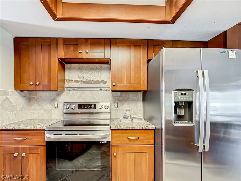 207 Redfish Road Fort Myers Beach, FL 33931 - Photo 7 of 50 a kitchen with stainless steel appliances granite countertop a refrigerator a stove and a sink with wooden cabinets