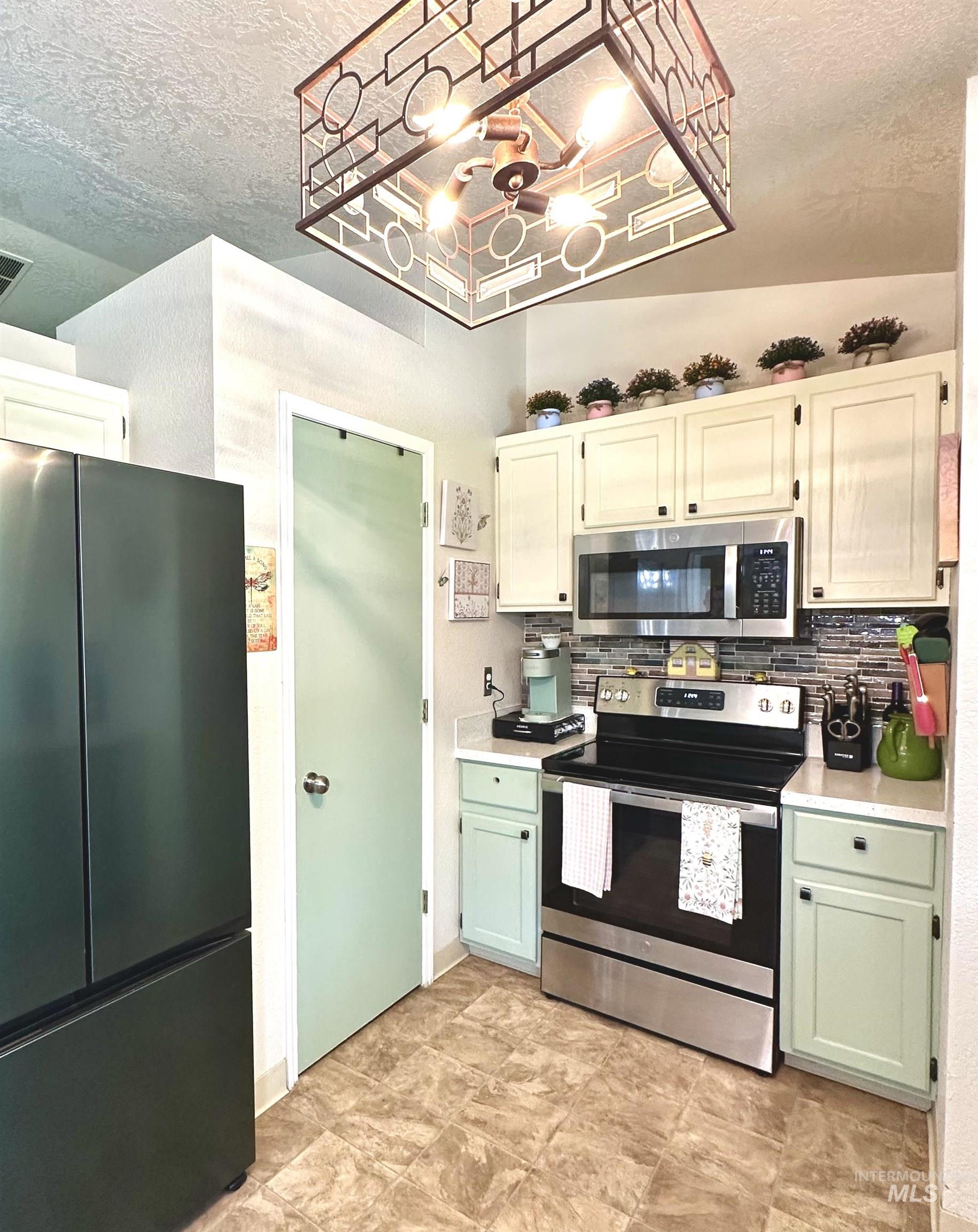 2472 North Maxie Way Meridian, ID 83646 - Photo 13 of 23 Kitchen featuring a black stainless steel refrigerator, stainless steel range and microwave, light-colored upper cabinetry, and light green lower cabinetry
