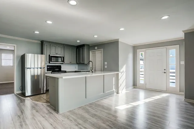 a kitchen with stainless steel appliances granite countertop a refrigerator a sink dishwasher a stove and white countertops with wooden floor