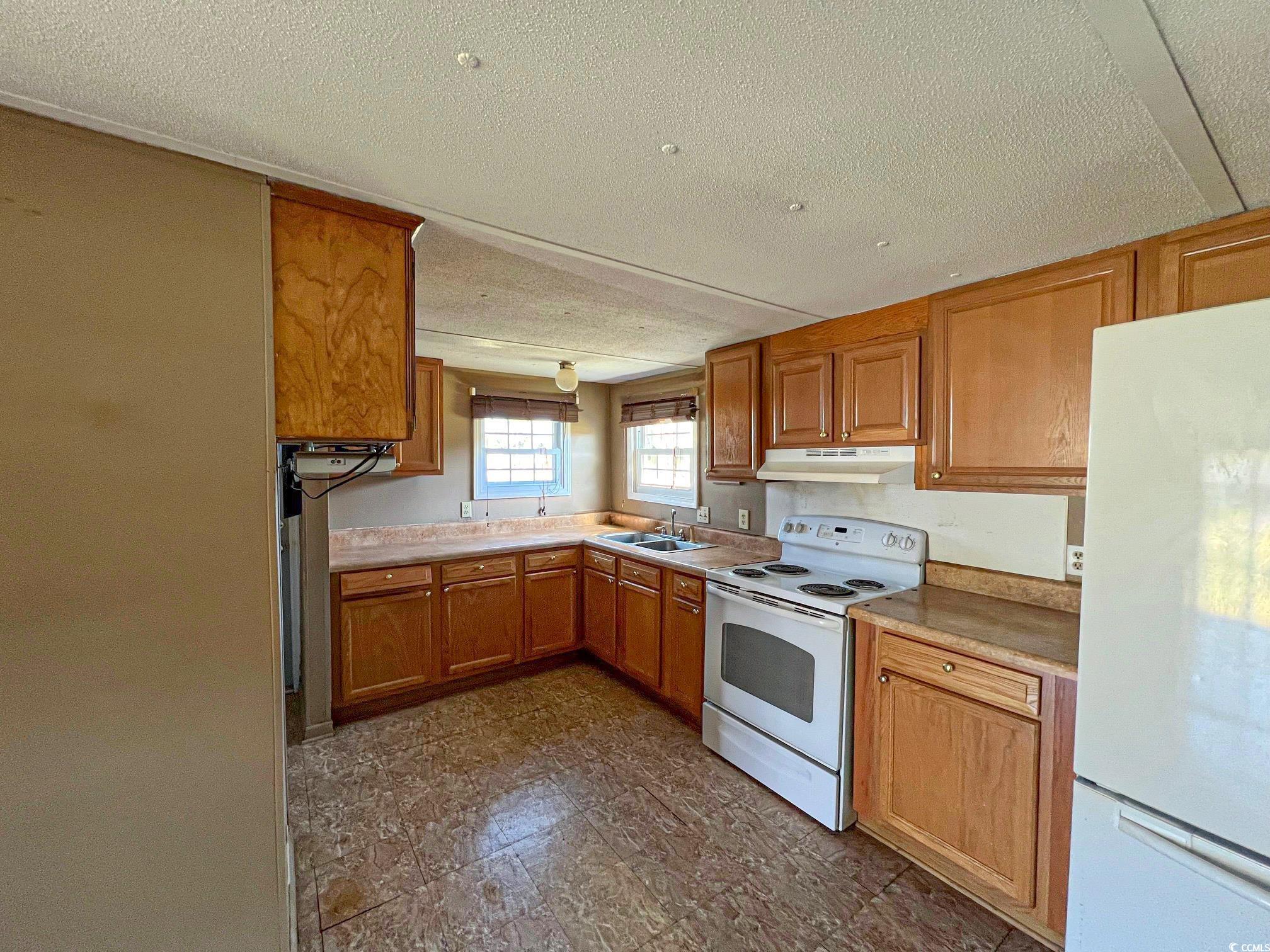 Kitchen featuring white appliances, a textured ceiling, and sink