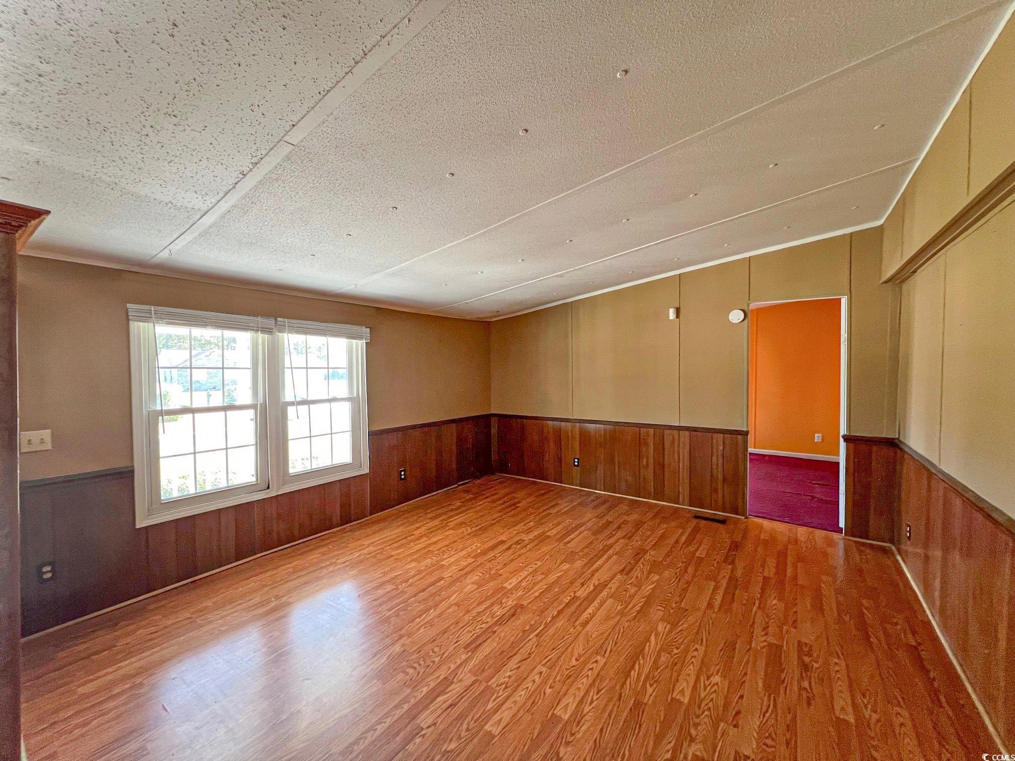Room with light hardwood / wood-style floors, wood walls, and a textured ceiling