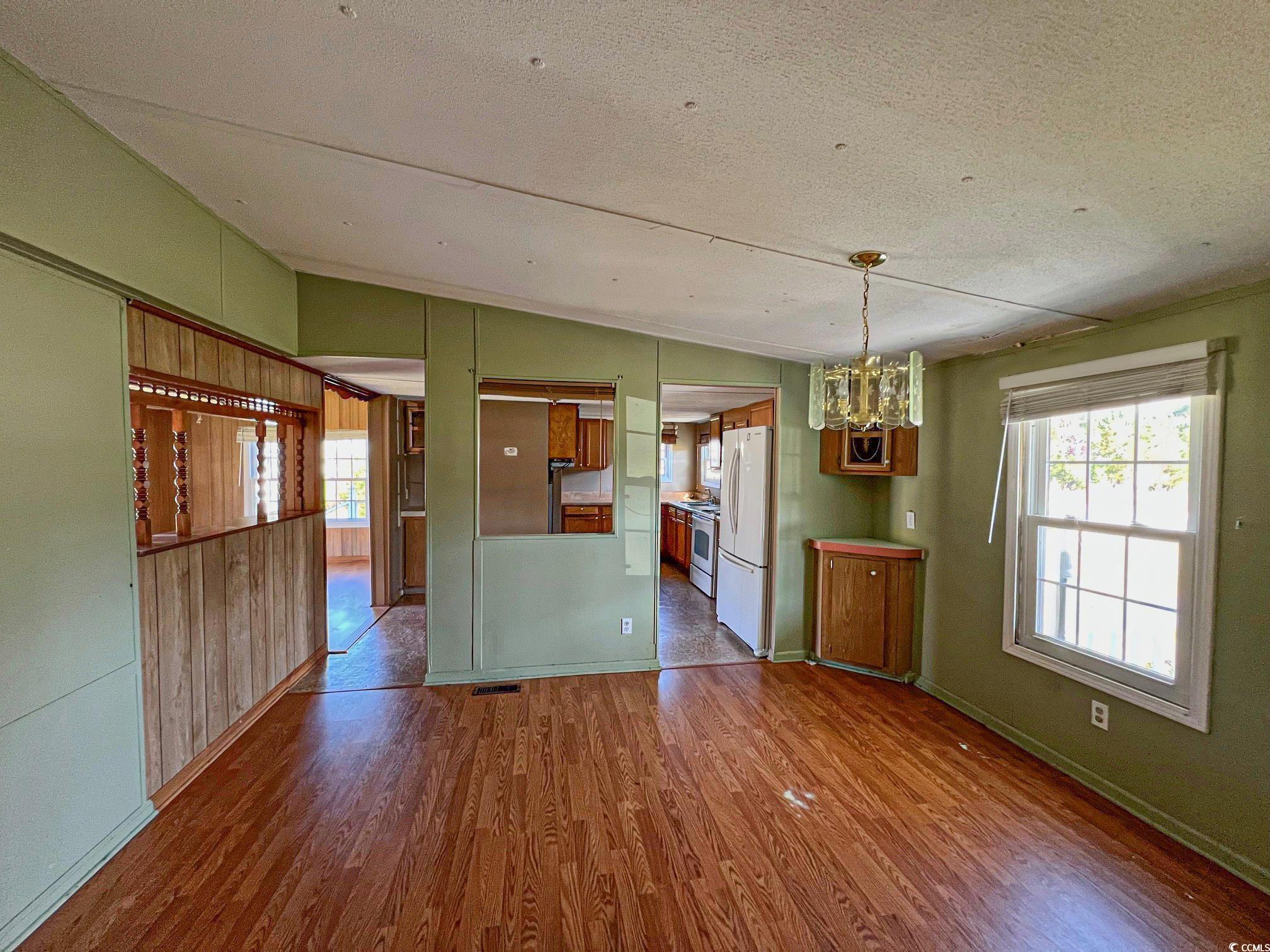 Unfurnished dining area with an inviting chandelier, wood-type flooring, vaulted ceiling, and a textured ceiling