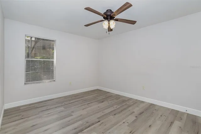 an empty room with wooden floor fan and windows