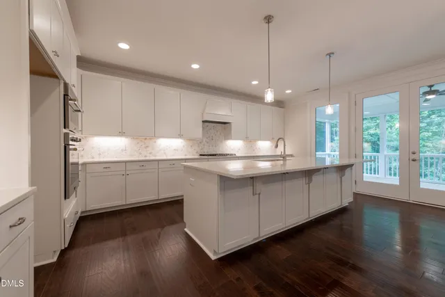 a kitchen with kitchen island granite countertop a stove a sink a refrigerator white cabinets and wooden floor next to a window