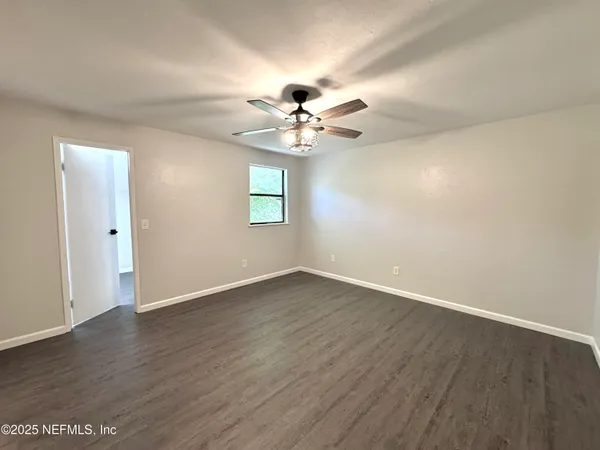 an empty room with wooden floor ceiling fan and windows