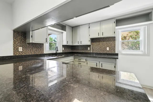 a kitchen with granite countertop a stove a sink and white cabinets