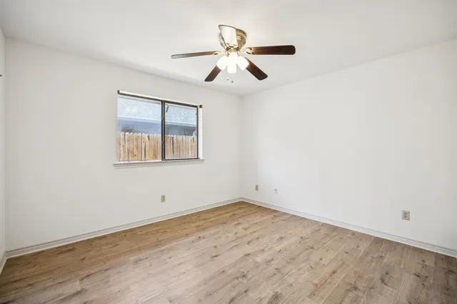 an empty room with wooden floor ceiling fan and windows