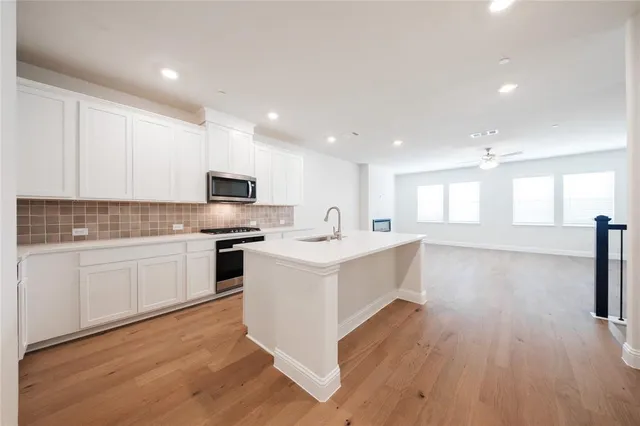a large white kitchen with kitchen island a sink wooden floor and stainless steel appliances