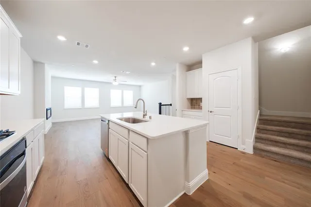 a open kitchen with white cabinets a sink dishwasher and a stove with wooden floor