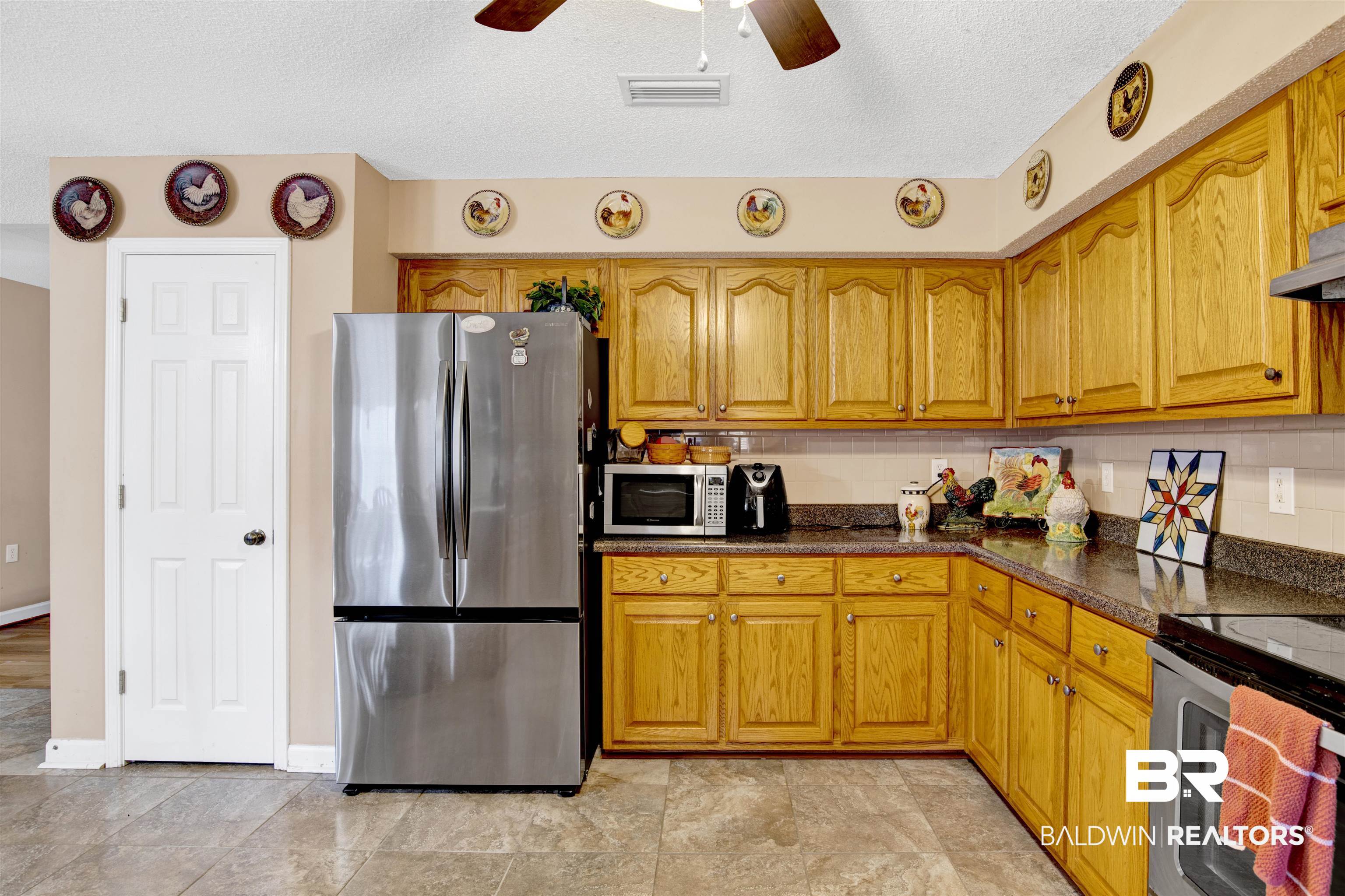 36434 Alexandria Trail Stapleton, AL 36578 - Photo 24 of 27 Kitchen with stainless steel appliances, a ceiling fan, a textured ceiling, brown cabinetry, and dark stone countertops