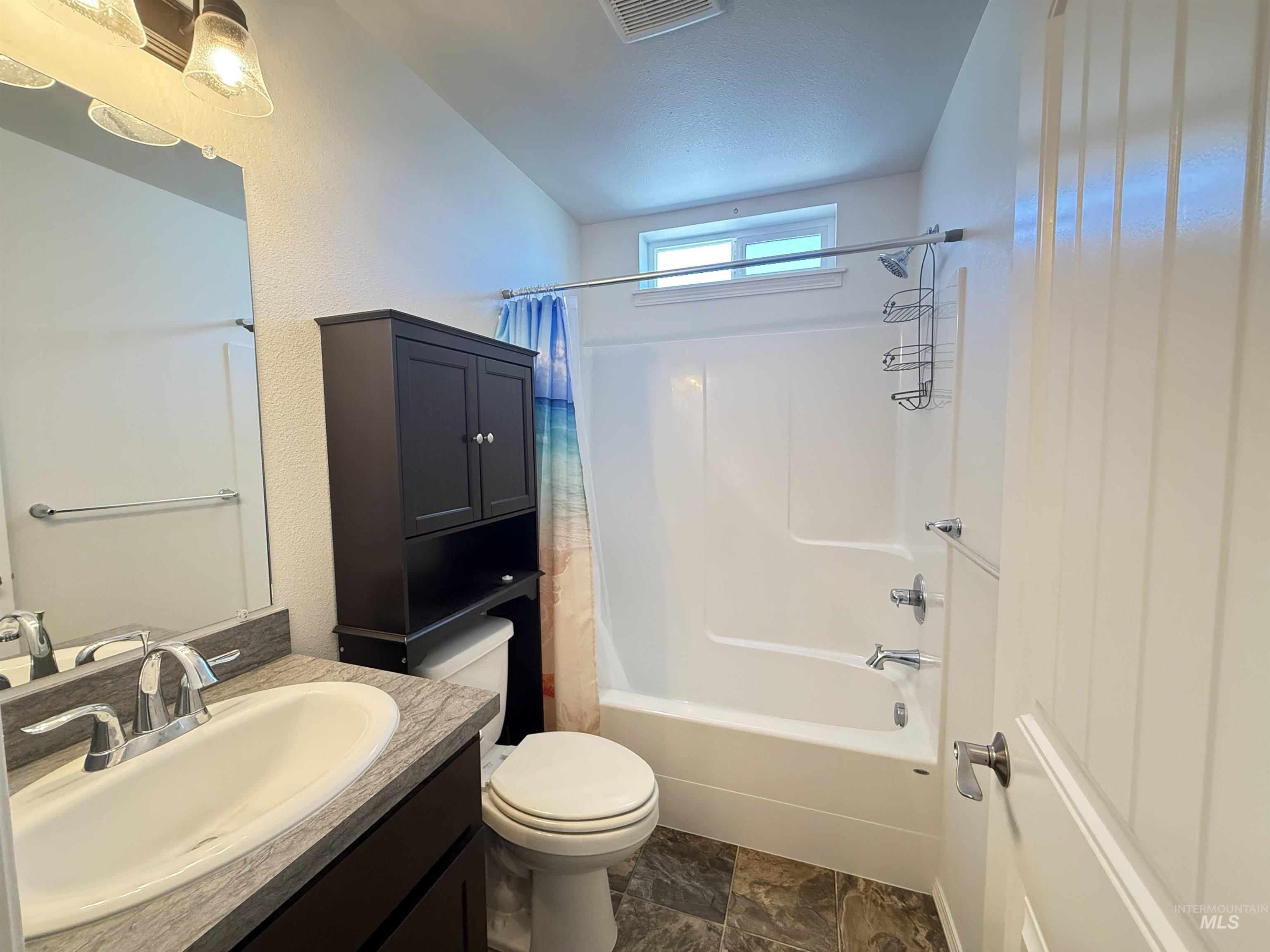 1556 Frontier Drive Lewiston, ID 83501 - Photo 23 of 23 Bathroom featuring a white bathtub/shower combination with a transom window, a dark wood-finish vanity with a single basin sink, a coordinating dark storage cabinet, and stone-look floor tiling