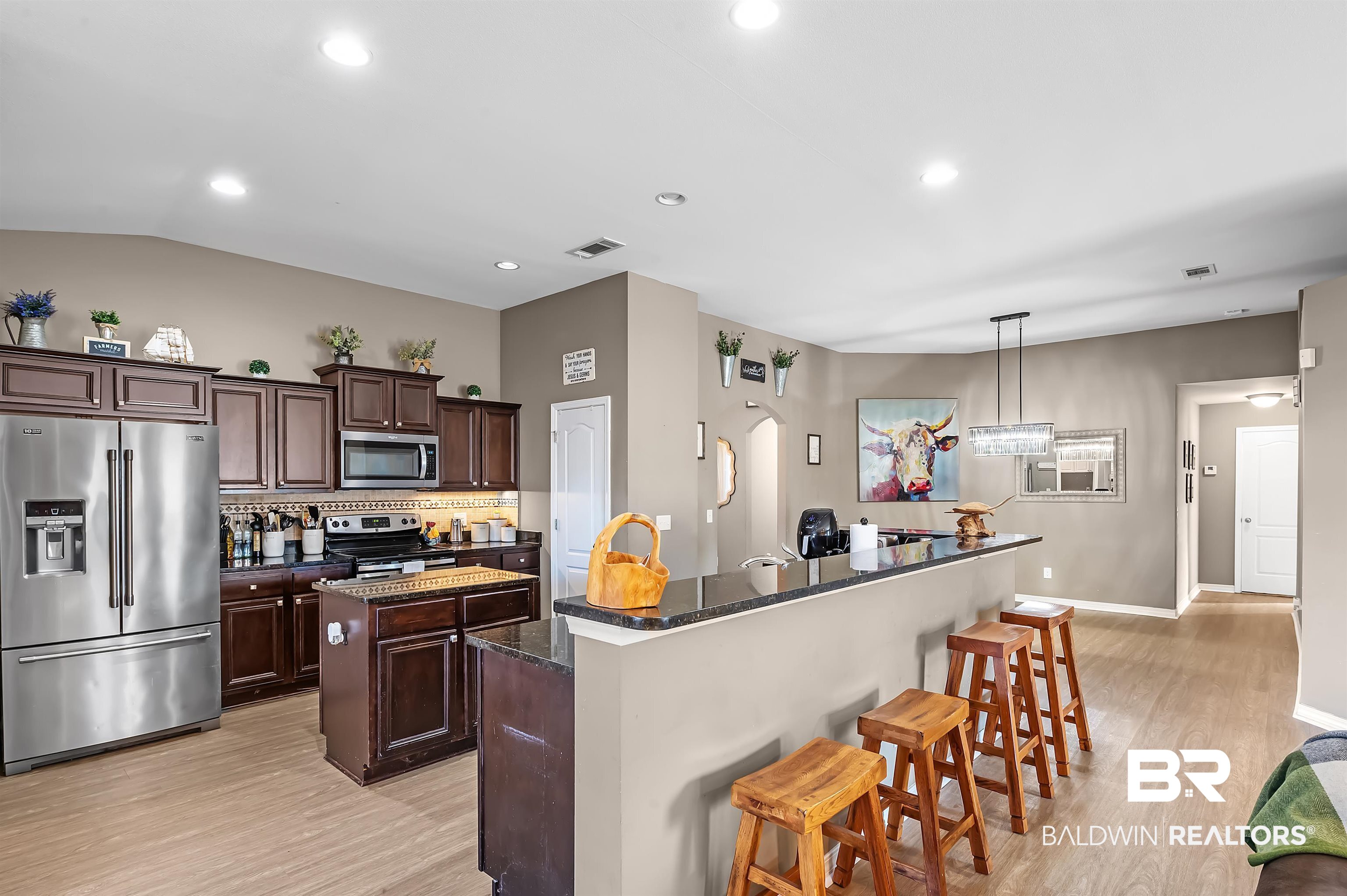 229 Meadow Run Loop East Foley, AL 36535 - Photo 17 of 31 Kitchen with hanging light fixtures, an island with sink, decorative backsplash, dark brown cabinets, and appliances with stainless steel finishes