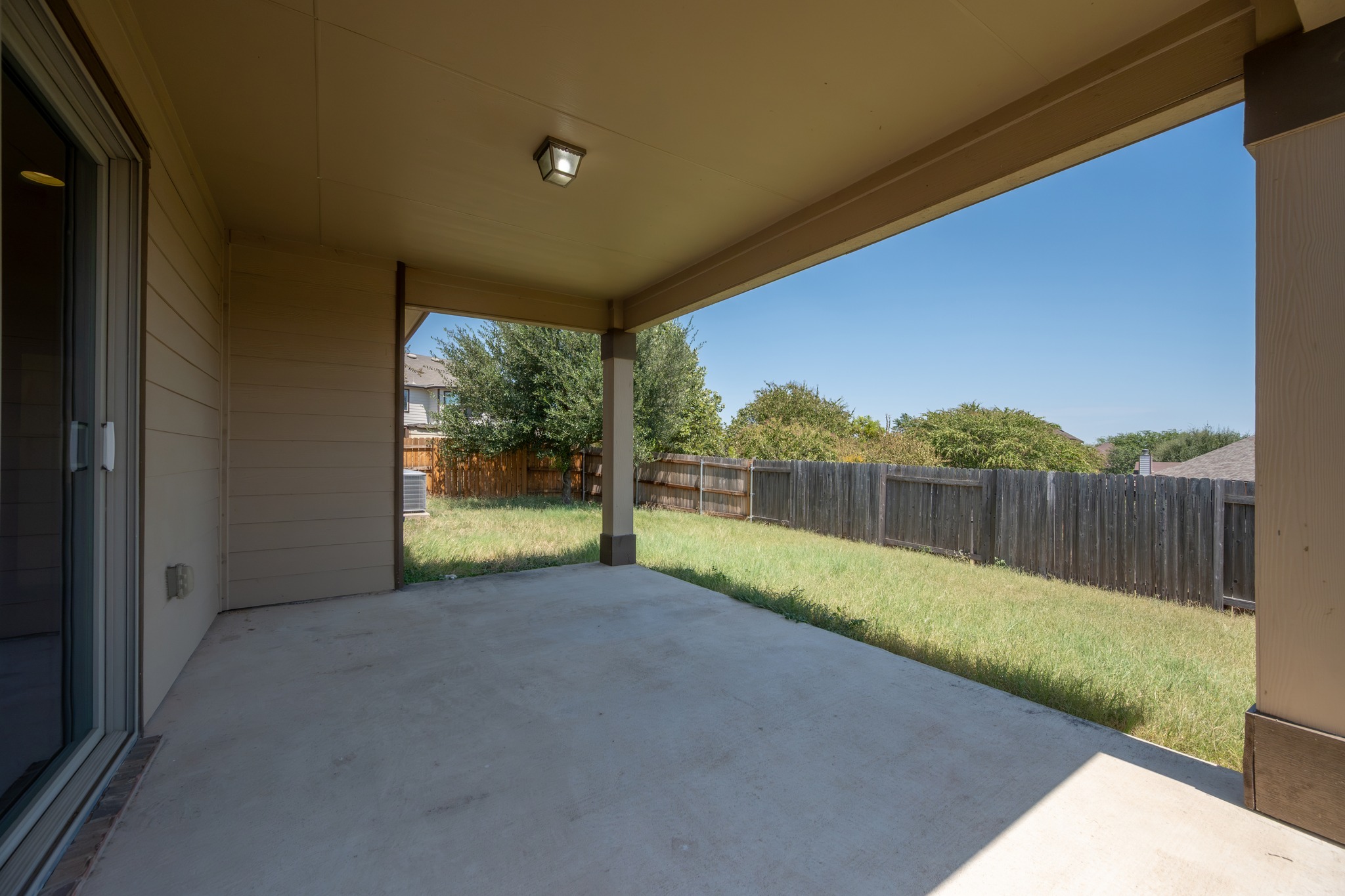 1141 Renaissance Trail Round Rock, TX 78665 - Photo 15 of 21 A covered concrete patio overlooks a fenced backyard under clear blue skies.