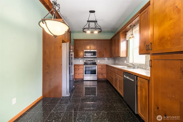 a kitchen with stainless steel appliances granite countertop a refrigerator a sink dishwasher a stove and a dining table with wooden floor