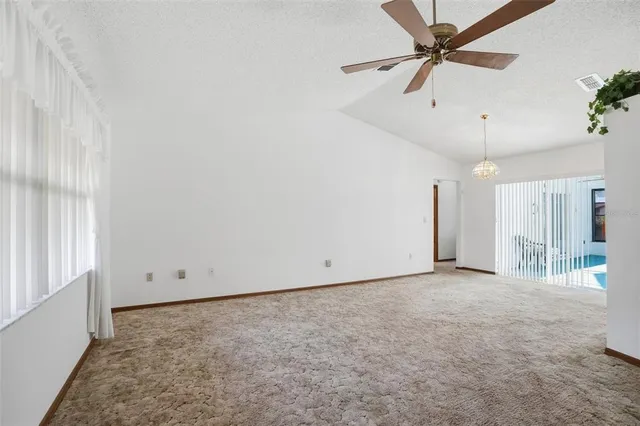 an empty room with chandelier fan and windows