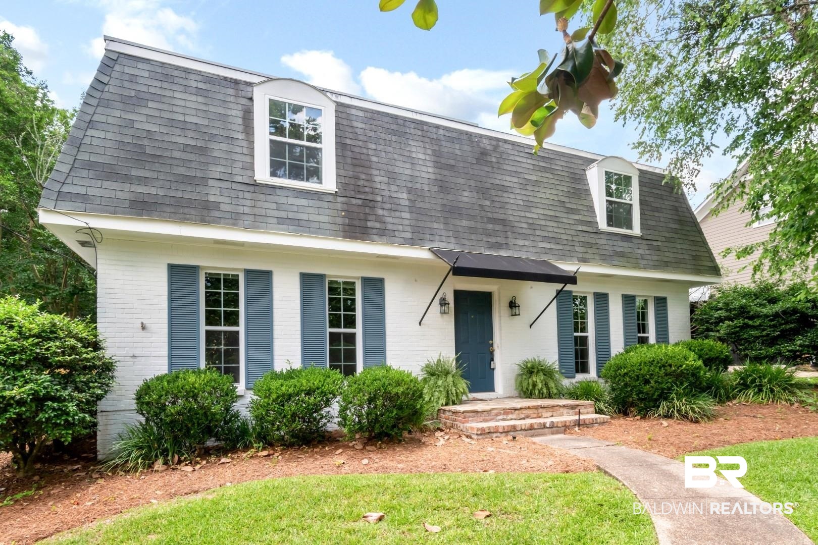 Colonial inspired home featuring mansard roof, brick siding, and a shingled roof