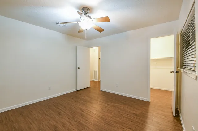 an empty room with wooden floor chandelier fan and windows