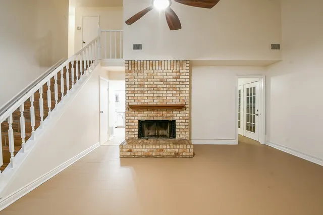 a view of an empty room with chandelier fan and fire place