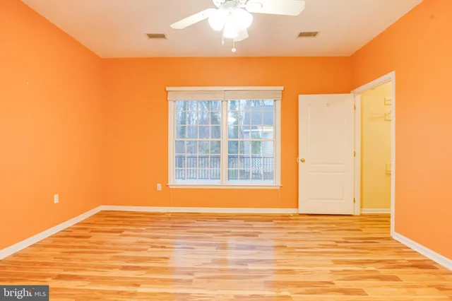 a view of an empty room with wooden floor and a ceiling fan