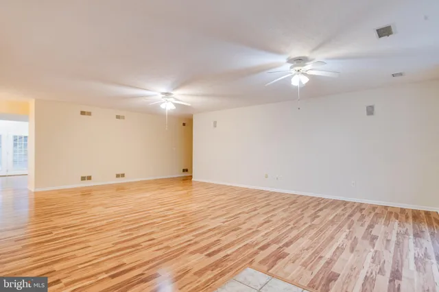 a view of an empty room with wooden floor and a ceiling fan