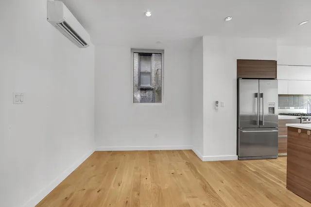 a view of empty room with wooden floor and kitchen