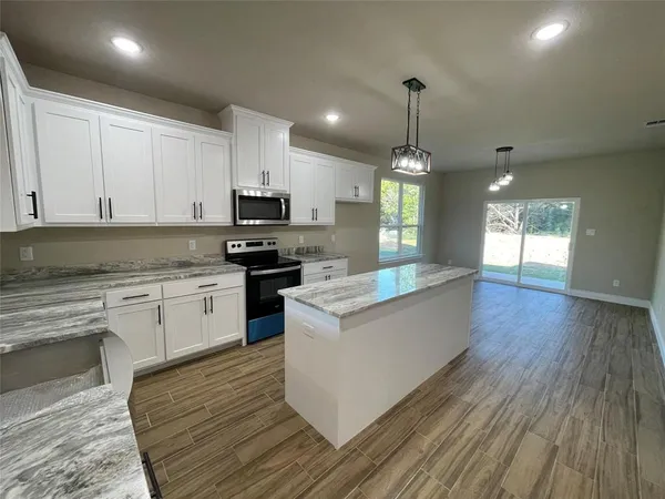 a large kitchen with granite countertop a stove top oven a sink dishwasher white cabinets and a wooden floor