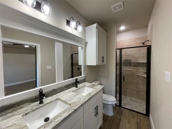 a bathroom with a granite countertop sink a toilet a mirror and shower