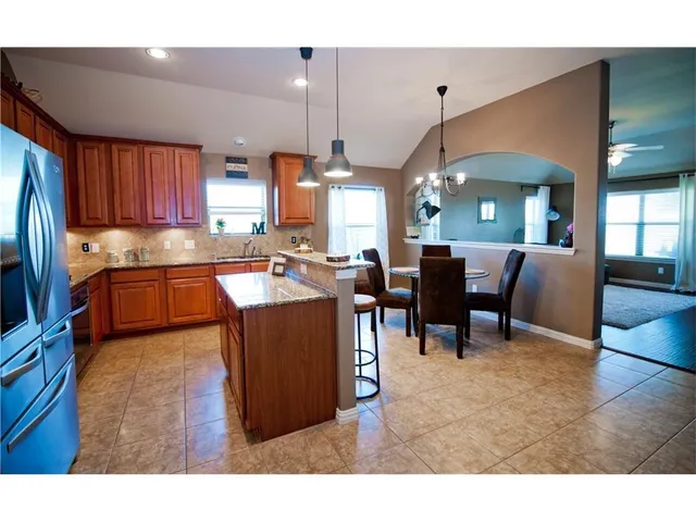 a kitchen with stainless steel appliances kitchen island granite countertop a dining table chairs and a refrigerator